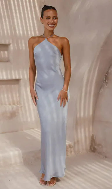 Woman wearing a light blue one-shoulder dress standing in a sunlit outdoor setting.