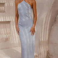 Woman wearing a light blue one-shoulder dress standing in a sunlit outdoor setting.