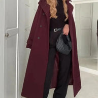 Person wearing a long burgundy coat in a room with white walls and a door.