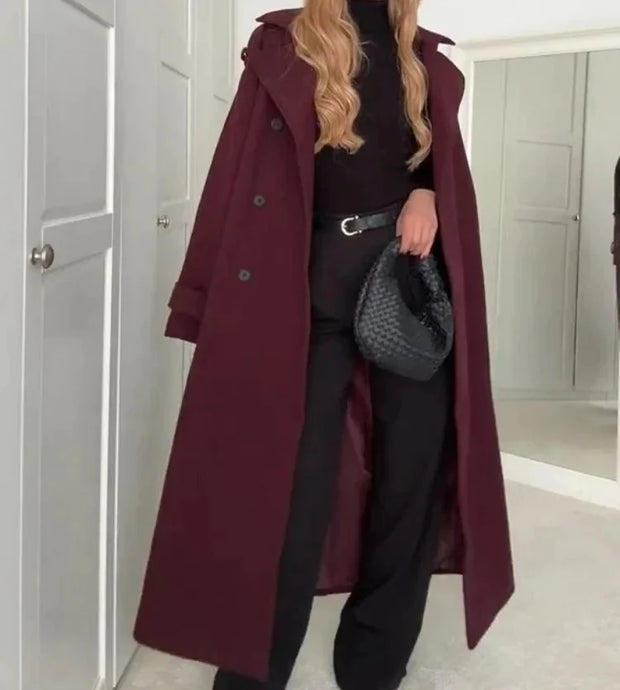 Person wearing a long burgundy coat in a room with white walls and a door.