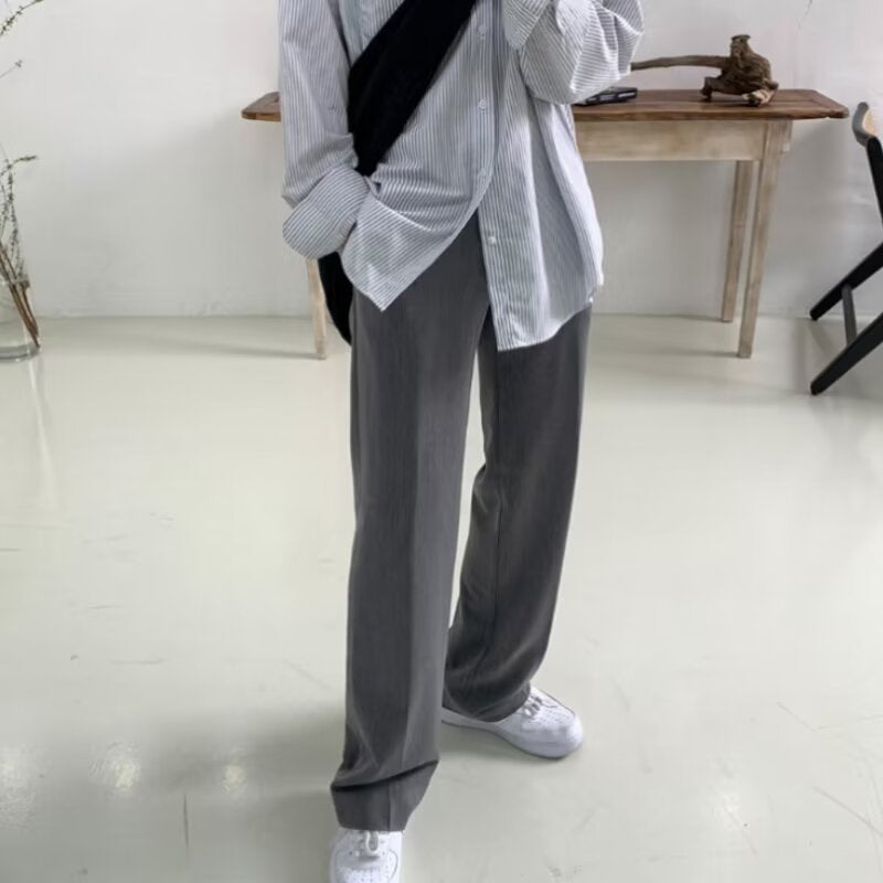 Person wearing a light-colored shirt and dark pants in a minimalistic room.