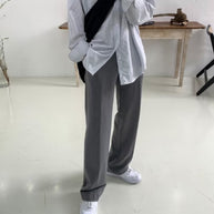 Person wearing a light-colored shirt and dark pants in a minimalistic room.