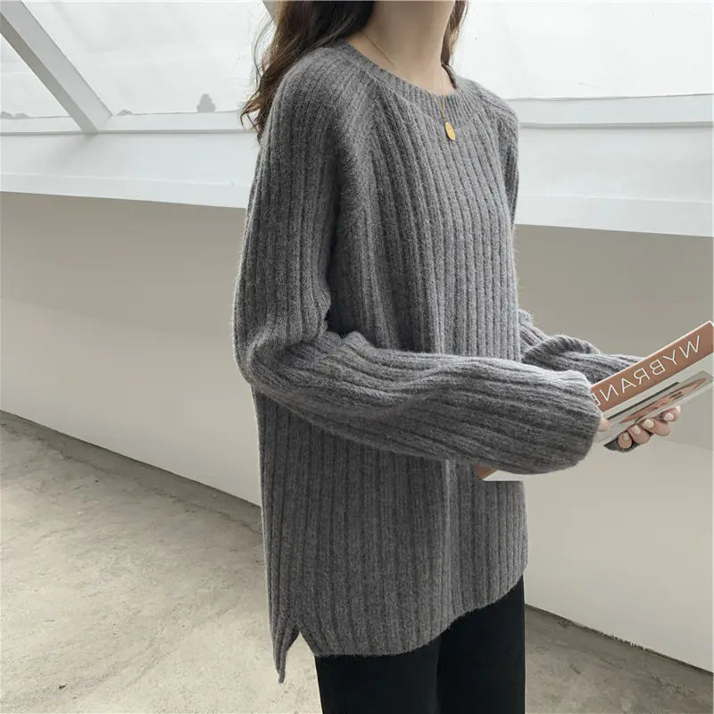 Person wearing a gray ribbed sweater holding a book indoors.