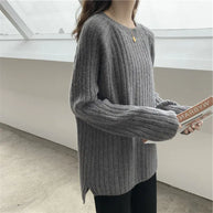 Person wearing a gray ribbed sweater holding a book indoors.