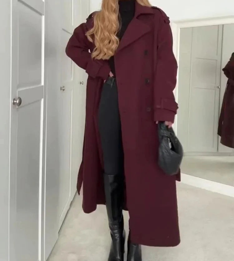 Person wearing a long burgundy coat in a room with white walls and a door.