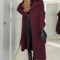 Person wearing a long burgundy coat in a room with white walls and a door.