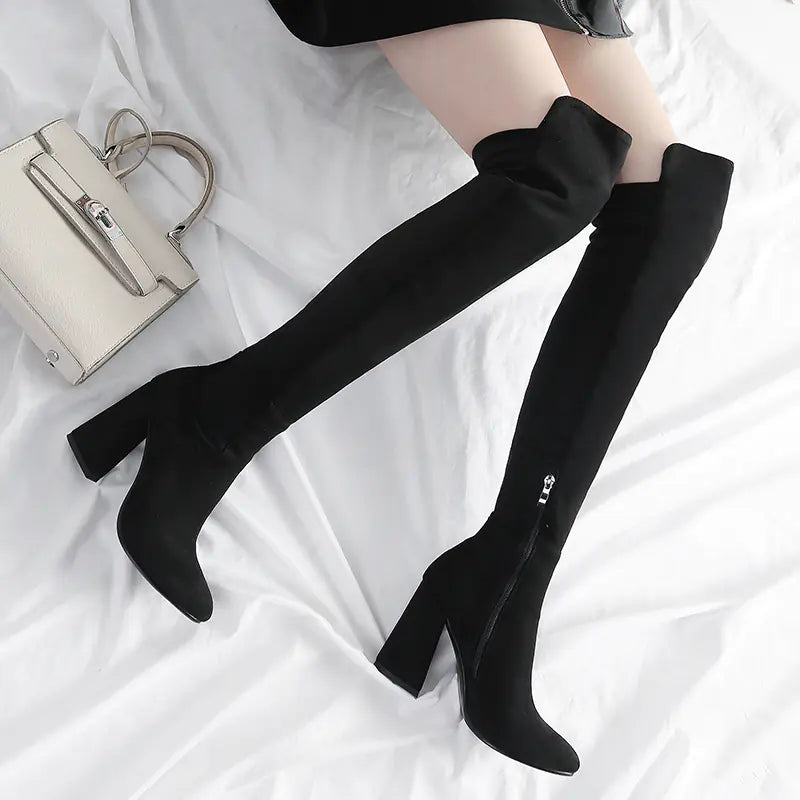 Black knee-high boots worn by a person on a white background with a small handbag.