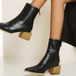 Black ankle boots with wooden soles worn by a person sitting on a white surface.
