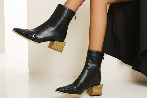 Black ankle boots with wooden soles worn by a person sitting on a white surface.