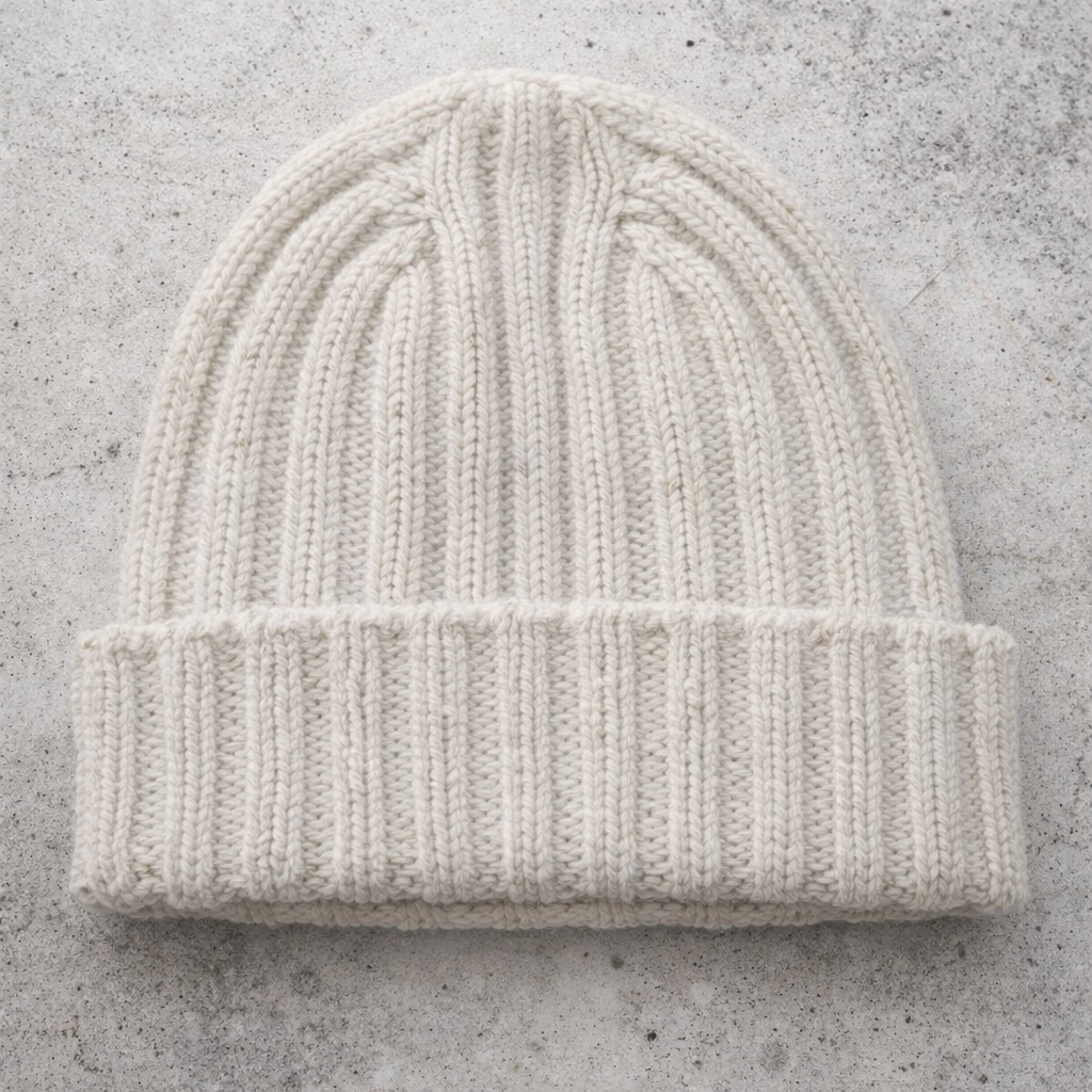 White knit beanie on a gray concrete surface
