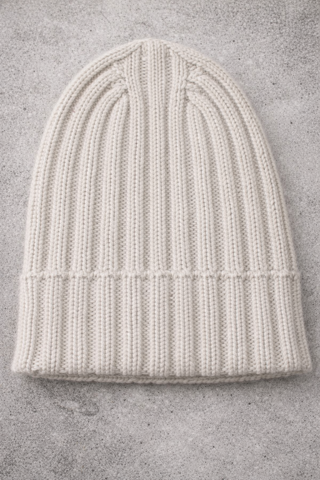 White knit beanie on a gray concrete surface
