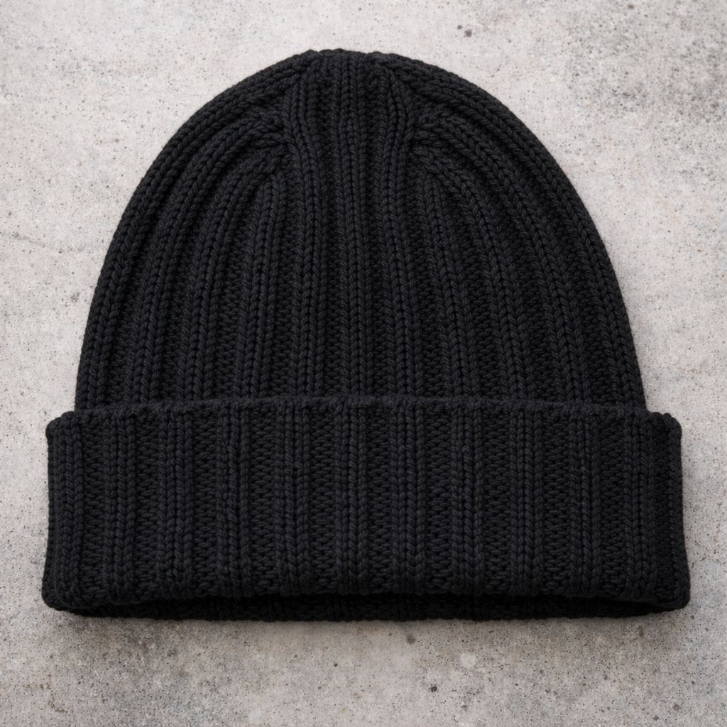 Black knit beanie on a light gray concrete surface