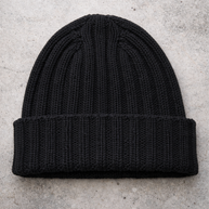 Black knit beanie on a light gray concrete surface