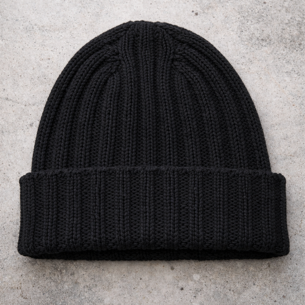 Black knit beanie on a light gray concrete surface