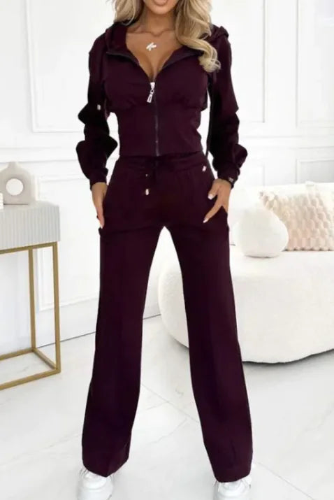 Woman wearing a dark purple tracksuit in a minimalistic room.