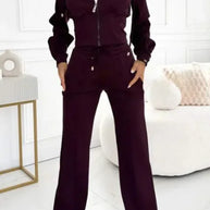 Woman wearing a dark purple tracksuit in a minimalistic room.