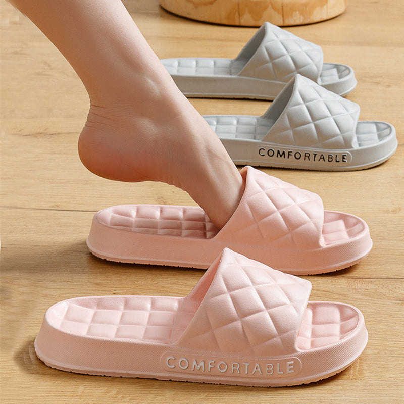 Pink and white quilted slide sandals on a wooden floor with 'COMFORTABLE' text.
