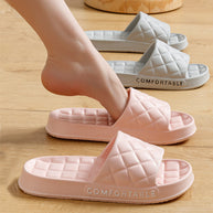 Pink and white quilted slide sandals on a wooden floor with 'COMFORTABLE' text.