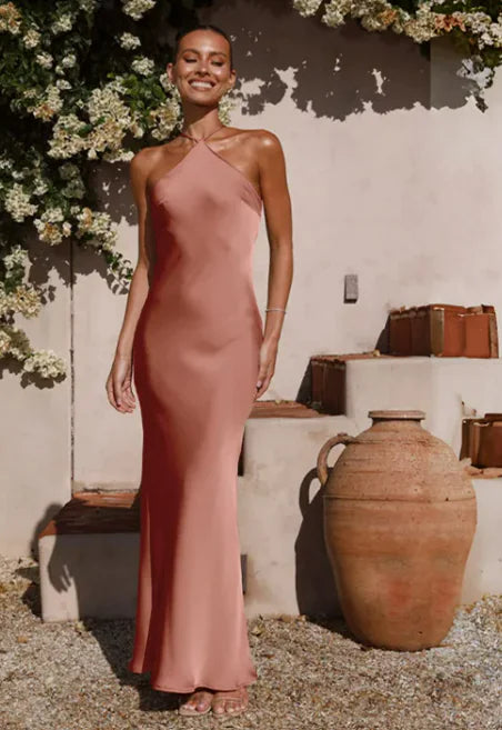 Woman in a pink dress standing outdoors with floral decorations and rustic vases.