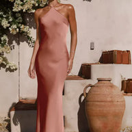 Woman in a pink dress standing outdoors with floral decorations and rustic vases.
